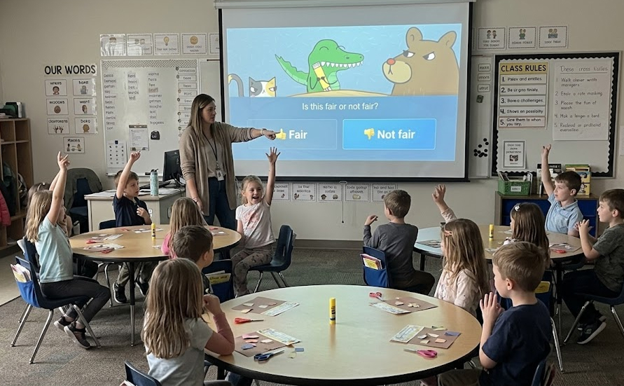 A classroom of kids watching the Fair or Not Fair Catbears game on screen while the teacher leads the discussion